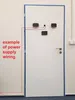 A white door with several electronic devices mounted on it, with a red line indicating power supply wiring. Produktbild-Vorschau