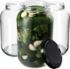 Three empty glass jars and one jar filled with pickles, dill, and garlic, with a black lid next to it. Podgląd zdjęcia produktu