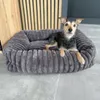 A small dog is lying in a plush gray dog bed. Produktbild-Vorschau