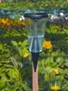 A rain gauge stands in a garden surrounded by green foliage and colorful flowers. Podgląd zdjęcia produktu