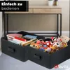 Two black storage boxes filled with books and toys, placed on a light gray surface in front of a desk. Náhľad obrázku produktu