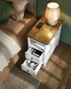 A bedside table next to a bed with a lamp and a phone charging on top. Náhled obrázku produktu