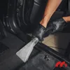 A person wearing black gloves is using a wet/dry vacuum cleaner with a specialized nozzle to clean the carpet inside a car. Produktbild-Vorschau