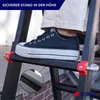 A person's foot wearing a black sneaker is stepping on a black ladder. The ladder has red accents and a close-up inset shows the textured surface of a ladder rung. Produktbild-Vorschau