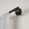 A close-up view of a black metal and wood curtain rod mounted on a white wall, with a sheer white curtain hanging from it. Podgląd zdjęcia produktu
