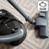 A close-up view of a black vacuum cleaner on a patterned carpet. Produktbild-Vorschau