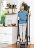 A woman is watering a plant while standing on a step stool in a kitchen. Náhled obrázku produktu