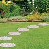 Stepping stones made of gravel are arranged on a green lawn in front of a garden bed with various flowers and plants. Produktbild-Vorschau