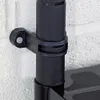 A close-up view of a black plastic bracket attached to a black pole, which is mounted to a textured white wall. Náhled obrázku produktu
