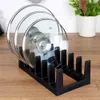 A black pot lid organizer holding three glass pot lids, placed on a wooden surface. Produktbild-Vorschau