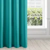 A close-up of a teal curtain hanging in front of a window with greenery visible outside. Produktbild-Vorschau