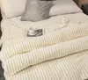 A close-up view of a cream-colored blanket with a ribbed texture, neatly folded on a bed with pillows. Podgląd zdjęcia produktu