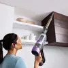 A woman is using a cordless stick vacuum cleaner to clean the ceiling area in a kitchen or pantry. Voir les images du produit