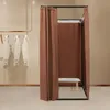 A freestanding changing room with brown curtains and a bench inside, with clothes hanging on a rack to the left. Voir les images du produit