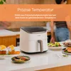 A white air fryer is shown on a kitchen counter with food items around it. Text overlays describe its features. Náhľad obrázku produktu