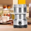 A coffee grinder is shown on a wooden table next to a cup of coffee and coffee beans, with a kitchen background. Náhled obrázku produktu