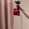 A hand holds a red and black handheld steamer near a pink curtain. Anteprima dell’immagine prodotto