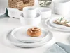 A table setting with white porcelain dishes, a cinnamon roll, and a napkin. Produktbild-Vorschau