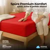 A person sitting on a red bed with a white blanket. Produktbild-Vorschau