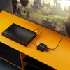 A black video capture box connected to a device and a TV, placed on an orange entertainment center. Náhled obrázku produktu