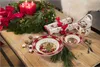 A festive Christmas table setting with a wreath, candles, crackers, mugs, and bowls. Produktbild-Vorschau