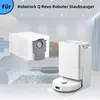 A white robot vacuum cleaner and its dust bag station are displayed in a modern living room setting. Produktbild-Vorschau