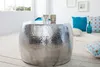 A silver hammered metal coffee table in a living room setting with pillows and a vase. Produktbild-Vorschau
