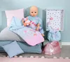 A baby doll is sitting on a stack of pillows with a sleeping bag and other accessories. Produktbild-Vorschau