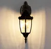 A classic outdoor wall lantern with a gold-colored mounting plate and a black lantern body with clear glass panels, mounted on a textured white wall. Voir les images du produit
