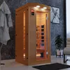 An infrared sauna cabin is shown in a modern room setting with a bathrobe hanging on a rack and a plant in a pot. Produktbild-Vorschau