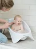 A baby is taking a bath in a white baby bathtub, with a person assisting. Produktbild-Vorschau
