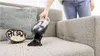 A person is using a handheld vacuum cleaner to clean popcorn off a sofa. Produktbild-Vorschau