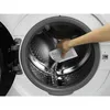 A hand is pouring a white powder from a sachet into the drum of a washing machine. Produktbild-Vorschau