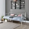 A white metal daybed with bedding is shown in a room with grey walls and a built-in shelf unit. Voir les images du produit