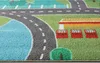 A close-up view of a children's play rug depicting a town with roads, a body of water, and buildings. Produktbild-Vorschau