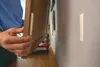 A person is attaching a picture frame to a wall using adhesive strips. Anteprima dell’immagine prodotto