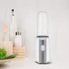 A white and silver mini blender with a clear bottle sits on a white surface, with kitchen items like a wooden spoon, a salt shaker, and a bowl of lettuce in the background. Produktbild-Vorschau