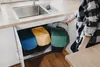 A person is reaching for a green trash can under a kitchen sink, next to two other trash cans. Podgląd zdjęcia produktu