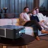 A family is watching a movie projected by a projector in a dimly lit living room. Anteprima dell’immagine prodotto