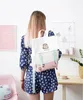 A young woman wearing a blue patterned outfit and carrying a Pusheen backpack in a room with pink and white decor. Anteprima dell’immagine prodotto
