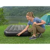 A woman is crouching and adjusting an air mattress next to a tent by a lake with a wooded hill in the background. Náhled obrázku produktu