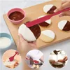 A collage of images showing a red silicone spatula being used for various kitchen tasks, including spreading frosting on cookies, spreading jam on toast, and drizzling chocolate on a cake. Produktbild-Vorschau