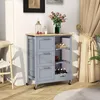 A grey kitchen cart with a wooden top is shown in a room with a chair and curtains. Podgląd zdjęcia produktu