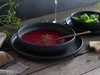 A dark bowl of beet soup with a spoon, a side bowl of salad, and bread on a wooden table. Náhľad obrázku produktu
