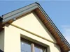 Close-up view of a house's gable end with a window and roof details against a clear blue sky. Produktbild-Vorschau