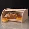 A wooden bread box with a roll-top lid, containing a large loaf of bread and two smaller rolls. Produktbild-Vorschau