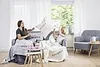 Two women are relaxing on a sofa, covered with blankets, in a living room setting. Produktbild-Vorschau