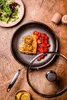 A cooked salmon fillet with cherry tomatoes and a side salad, presented on a wooden table with a frying pan and its lid. Náhled obrázku produktu