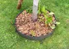 A tree ring made of Corten steel is placed around the base of a tree, filled with wood chips and some small plants. Produktbild-Vorschau