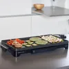 A close-up shot of an electric grill with food cooking on it, placed on a kitchen counter. Podgląd zdjęcia produktu